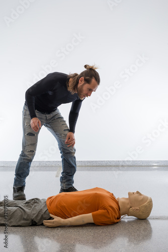 Man teaching cardiopulmonary resuscitation with a dummy on a white background. Doll lying on the floor, accident assessment.