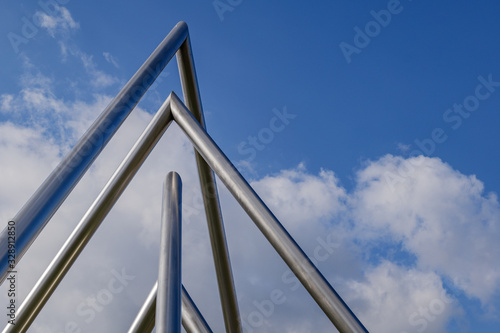 Conceptual abstract sculpture of triangular metal chrome pipes against deep blue sky.