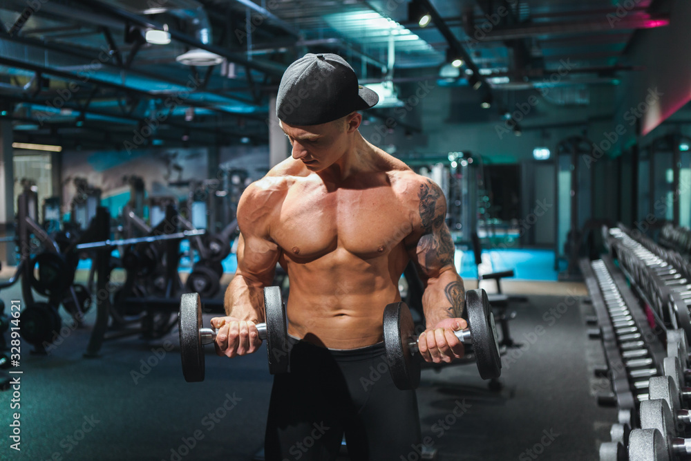 Naklejka premium Fit young man in sportswear focused on lifting a dumbbell during an exercise class in a gym