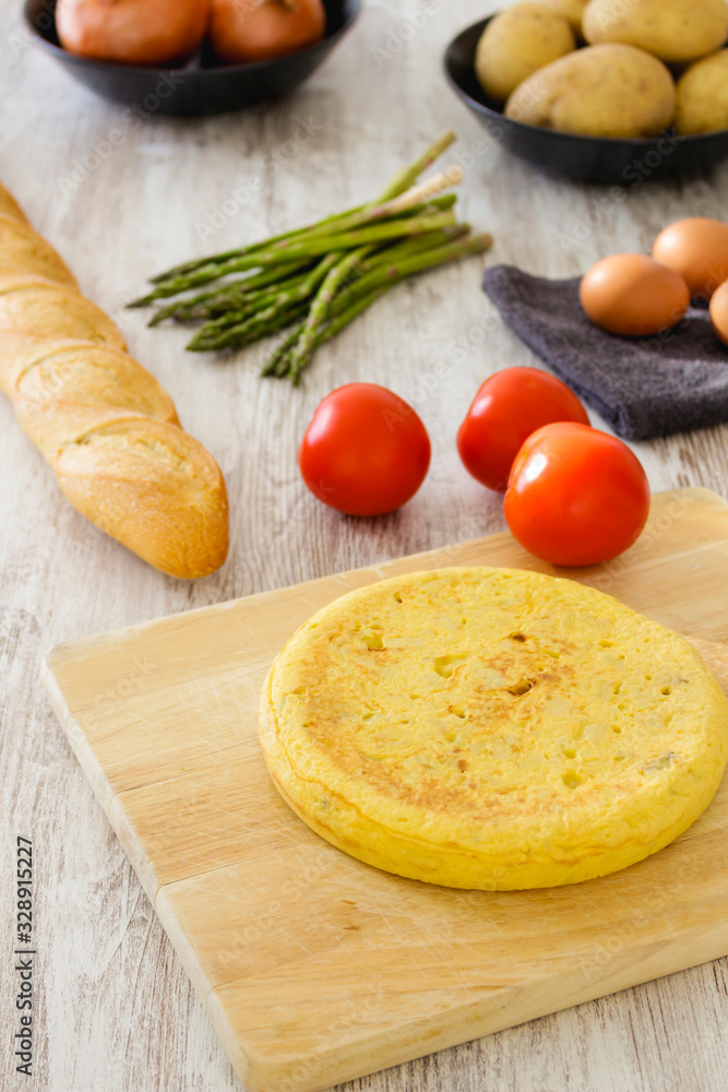 Potato omelette as a typical Spanish dish along with different healthy and vegetarian ingredients such as tomatoes, onions, eggs or asparagus, accompanied by a handmade loaf of bread, selective focus Potato omelette as a typical Spanish dish along with different healthy and vegetarian ingredients such as tomatoes, onions, eggs or asparagus, accompanied by a handmade loaf of bread, selective focus