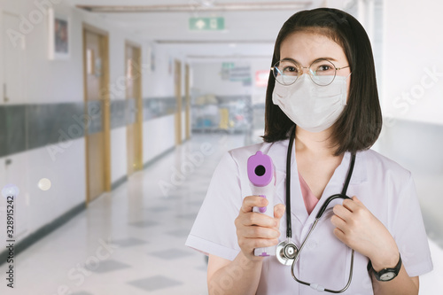 a woman doctor in a white coat holding an digital infrared thermometer in hospital