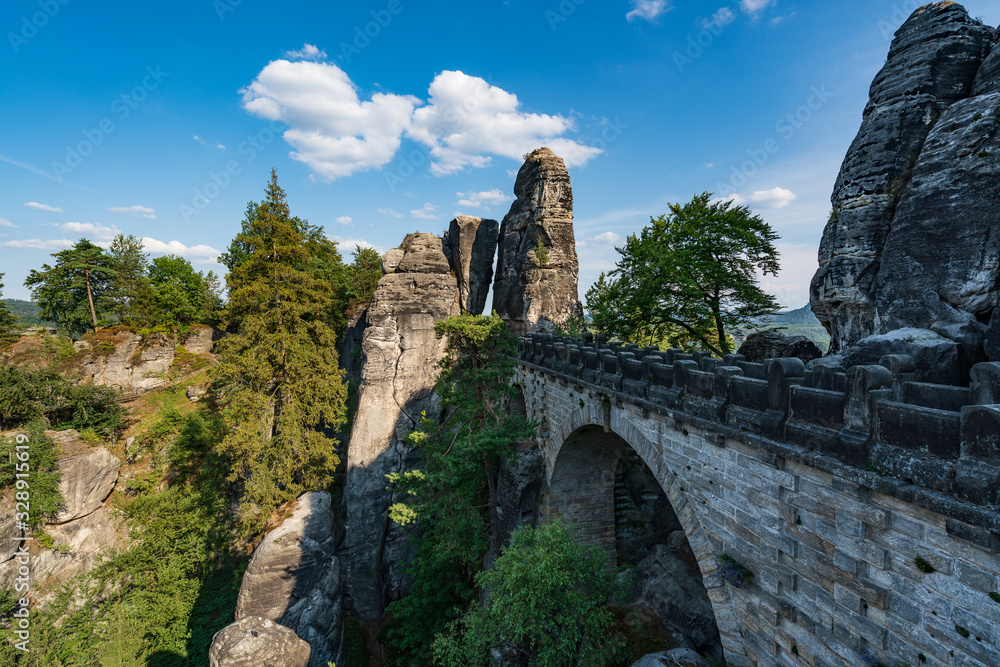 Bad Schandau in Bohemian Switzerland. Bastei bridge and mountain view. Narrow rock, natural sandstone arch in Europe..Hill scenery with greenery, blue sky and sunlight.