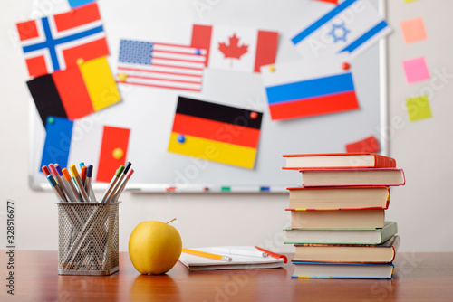 Stack of books, pencils, an apple in front of school whiteboard with flags of different countries. Concept of intercultural awareness