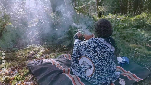 Woman shaman on a blanket burning plant medicine in a clay bowl talking with her ancestors photo