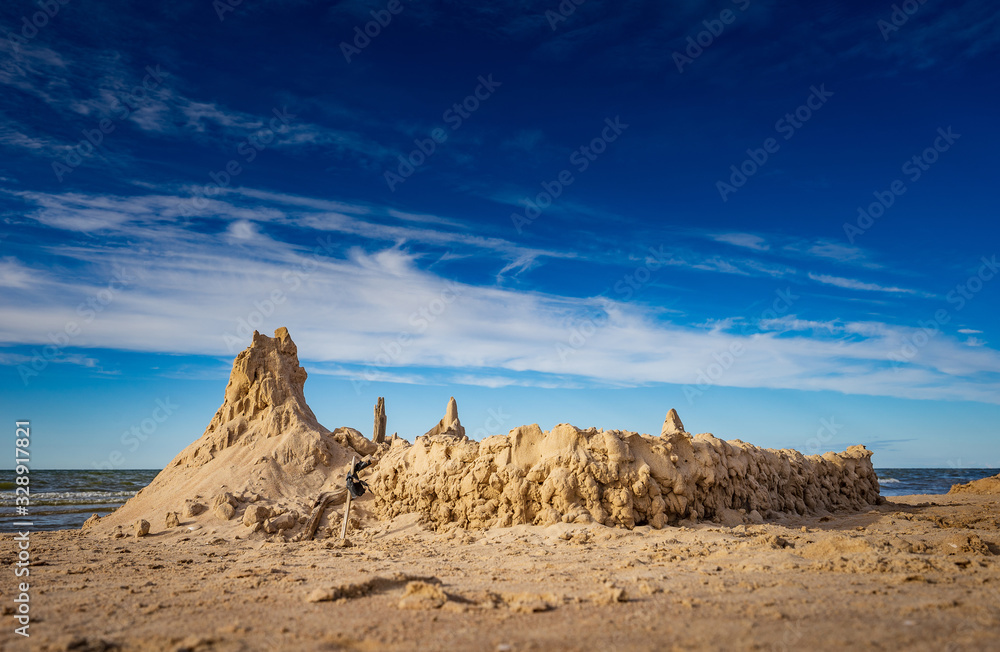 Sand castle on beach on sunset. A sandcastle on a sandy coast, blue sky. House with high towers on sandy shore.