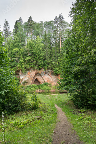 Sand stone cliffs and Salaca river. Red sandstones cave, water, trees and plants, green nature environment, climate concept..Angels cliff in Mazsalaca nature park, Latvia, Europe photo