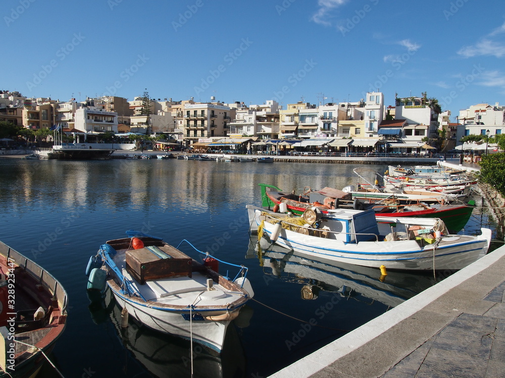 A small Mediterranean marina with fishing boats and light colored buildings in the background