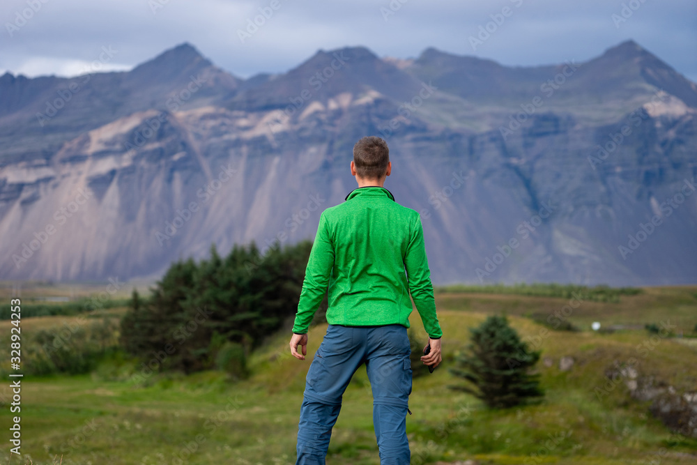 Backside of tall caucasian man wearing green jacket standing in over mountain and fog background. Promoting healthy lifestyle Backside of tall caucasian man wearing green jacket standing in over mountain and fog background. Promoting healthy lifestyle