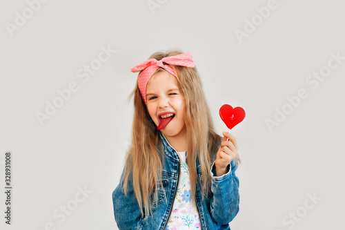 Portrait of a beautiful stylish fashionable girl in glasses, with a heart-shaped lollipop, on a white background, free time summer vacation #328931008