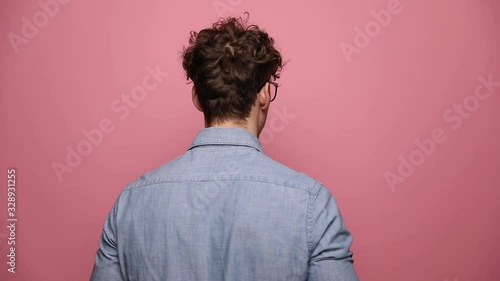 young casual man wearing glasses posing in rear view then turning in side view and smiling happy finally turning in front view and giving a thumbs up on pink studio background