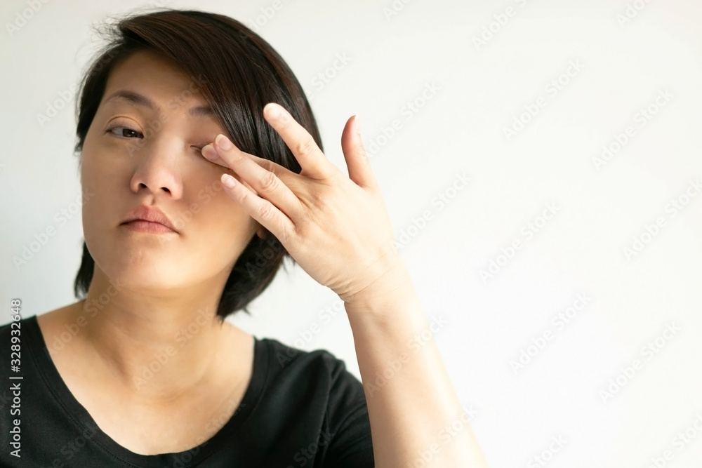An Asian woman uses a finger to wipe her eye on white background. An Asian woman uses a finger to wipe her eye on white background.