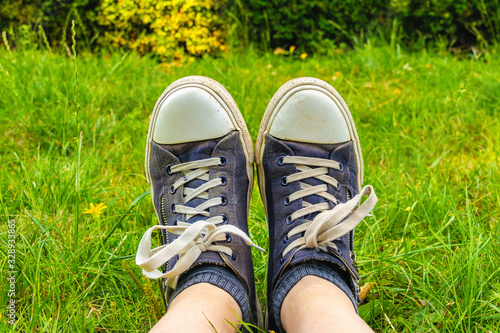 Legs in old, dirty, shabby sneakers on the green grass. Tourist and travel concept. © Olga Soloveva
