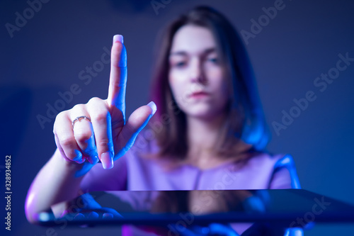 Woman with a tablet. Girl shows a finger. Studenka shows a hand gesture. Student wants to click on the tablet. Young woman on a dark background. Concept - Using Gadgets. Concept - study with a tablet photo