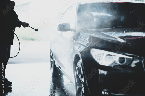 Silhouette of hands of a man washing black car outdoors in a carwash station, using water jet with high pressured water stream
