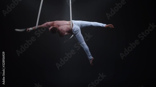 Muscular circus aerialist on the aerial straps in black studio photo