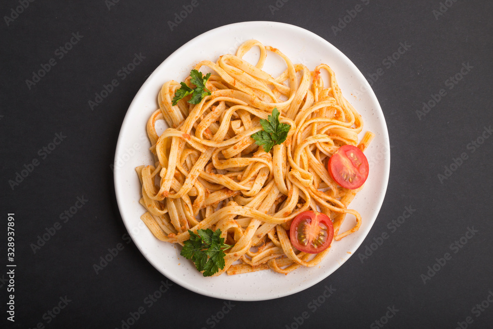 Semolina pasta with tomato pesto sauce, orange and herbs on a black background. Top view. Semolina pasta with tomato pesto sauce, orange and herbs on a black background. Top view.