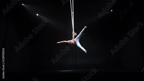 4k Muscular circus aerialist on the aerial straps in black studio photo