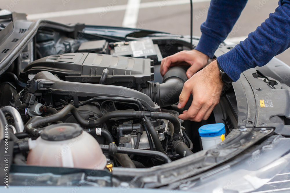 Closeup of mechanic hands checking motor under the hood in the broken car. Repairing of the vehicle concept. Automobile service