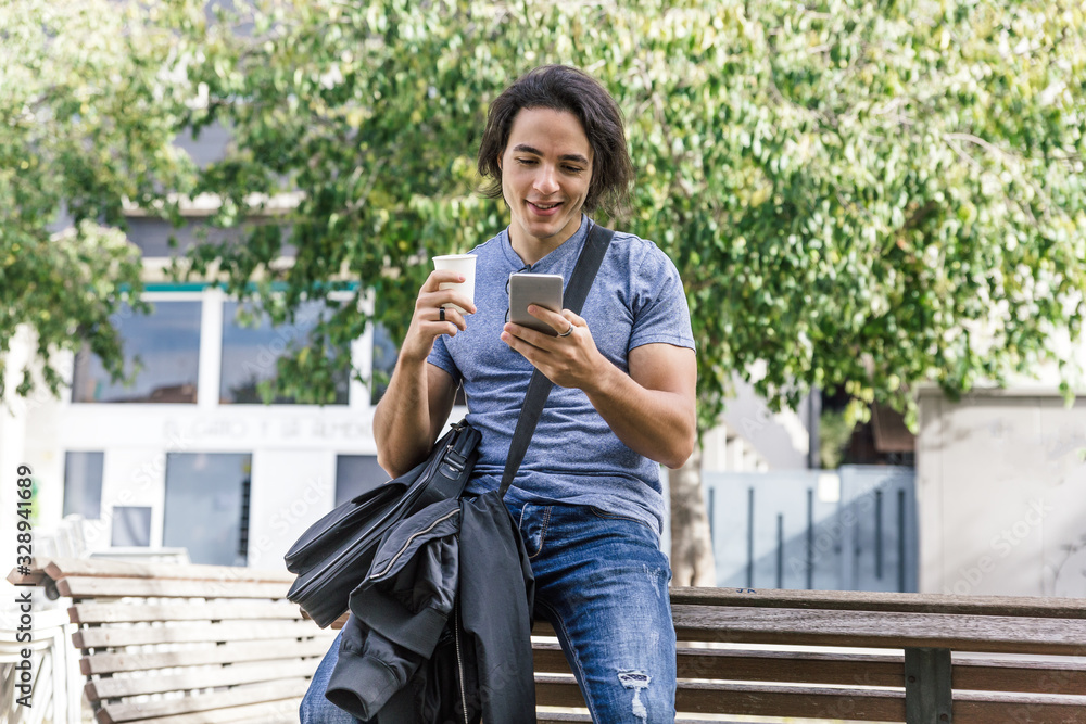Obraz premium Long haired caucasian boy with blue casual clothes smiles as he looks at his cell phone