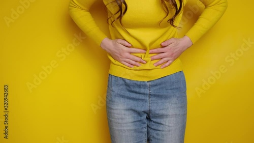Cropped close up view girl touch stomach suffers from severe ache, keeps both hands on belly, twinges of pain caused by menstrual period, gastric ulcer, wears sweater, isolated on yellow background