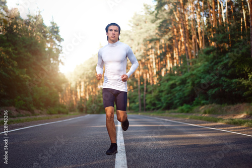 Caucasian middle age man athlete runs sunny summer day on asphalt road in the forest.