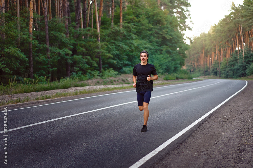 Caucasian middle age man athlete runs sunny summer day on asphalt road in the forest. Caucasian middle age man athlete runs sunny summer day on asphalt road in the forest.