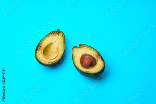 A rotten avocado cut in half on blue background. One slice with core.