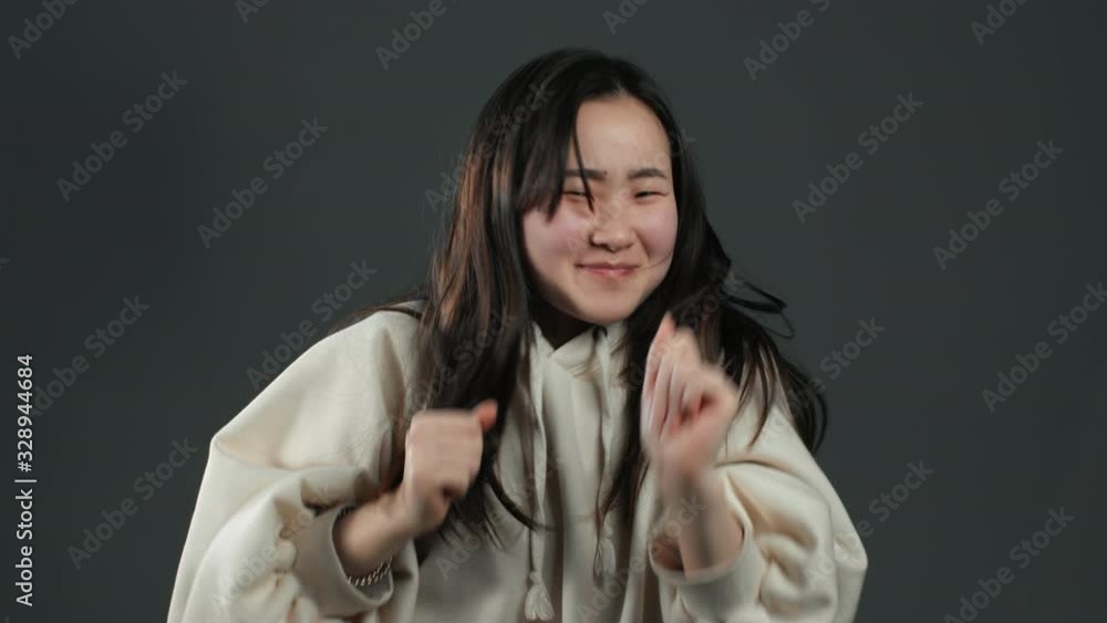 Funny asian woman with long hair having fun, smiling, dancing in studio against grey background. Music, dance concept, slow motion Funny asian woman with long hair having fun, smiling, dancing in studio against grey background. Music, dance concept, slow motion