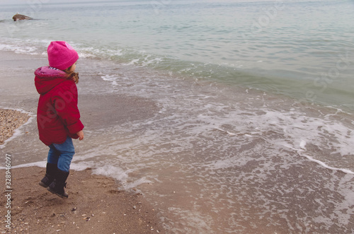 little girl in a red jacket plays with the waves on the beach