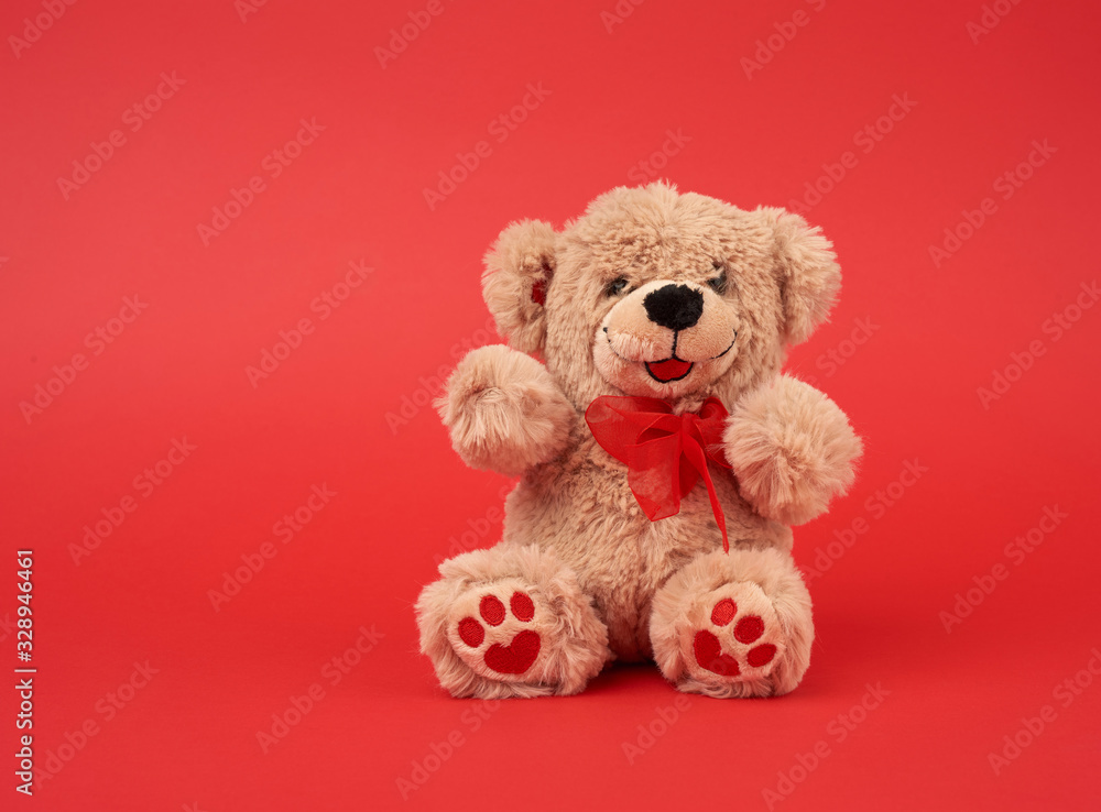 cute little brown teddy bear, toy is sitting on a red background cute little brown teddy bear, toy is sitting on a red background