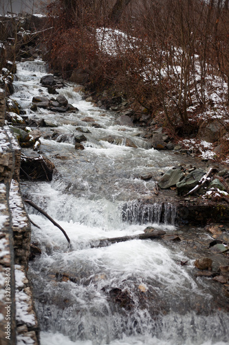 A mountain river flows over stones. River in the mountains in winter. A stream of water along a rocky slope. Clear water from a glacier flows along a rocky bottom.