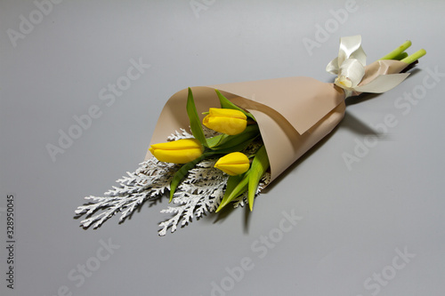 Minimalistic spring bouquet of unblown yellow tulips and conferen on a gray background, selective focus photo