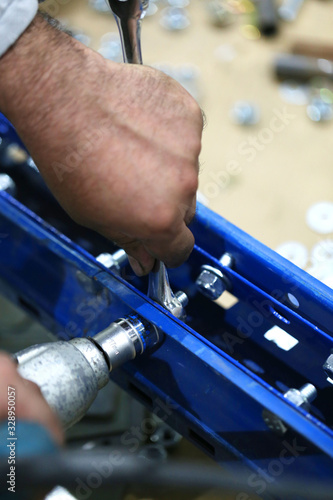 Fotografie One warehouse worker in with power tool tightening screw during rack arrangement