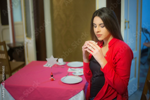 Bellissima donna italiana brunetta con capelli lunghi maglietta e camicia rossa nera in interno al momento della colazione beve un caffè al tavolo  photo