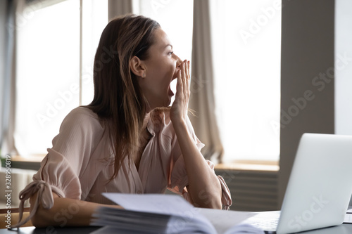Head shot distracted from work study young woman yawning, having lack of energy during workday at home or office. Tired businesswoman feeling bored, looking at window, chronic fatigue concept. photo