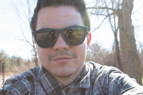 Handsome stylish man in hipster plaid shirt and sunglasses posing near sea side at sunshine, enjoying beautiful view and relax near ocean.