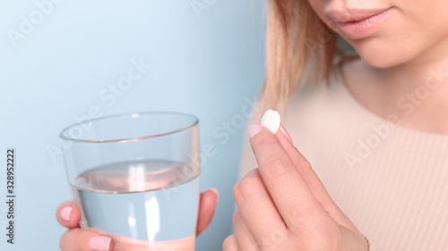 Close up of unhealthy young woman taking in pill and glass of water. Blue background. 
