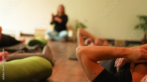 Shallow depth of field of senior woman lying on yoga mat holding breast while doing hand rotation exercise with a group of people