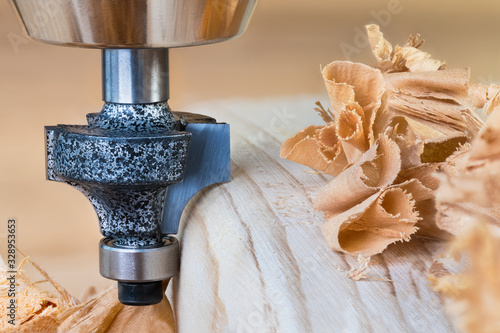 Shaping copying shank router bit clamped in chuck of a working machine tool. Sharp steel woodworking milling cutter with bearing forming a round edge on wood plank. Pile of twisted shavings. Joinery.