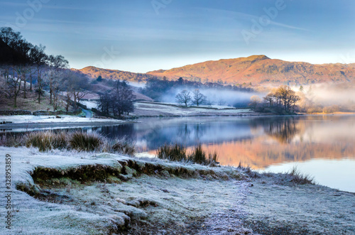 A morning scene with reflections of the frost and mist lifting from Grasmere lake in the Lake District