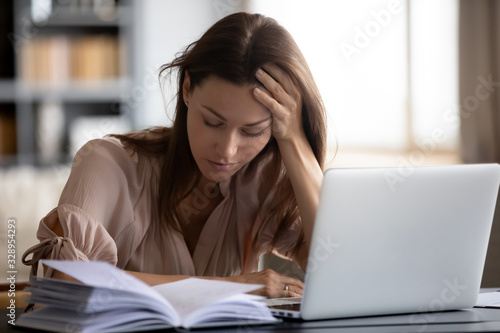 Obraz na płótnie Head shot exhausted female student holding head in hand, tired of monotonous study alone at home
