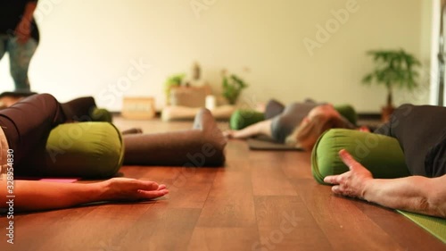 Selective focus of group of female lying in corpse pose with knees resting on bolster and palms facing upwards, at yoga session to cure breast cancer