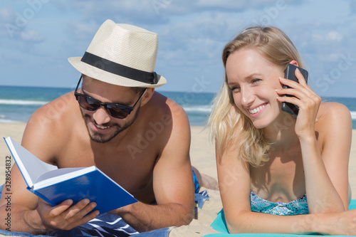 young couple relaxing on the beach with book and phone