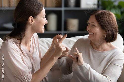 Fotografi Head shot pleasant young dumb woman communicating nonverbal with deaf middle aged lady, sitting together on couch
