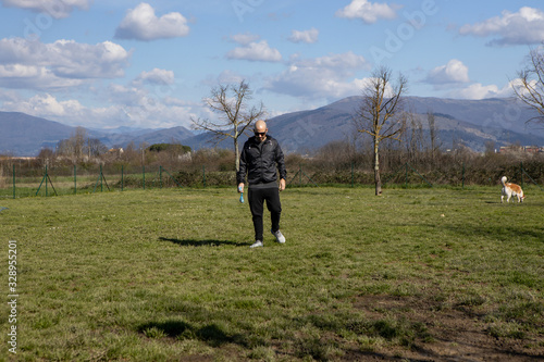 Man picking up and cleaning up dog poop in a dog area, with mountains, blue sky and clouds on the background. Caucasian guy picks up his dog's poop from a park. Concept of clean area and park