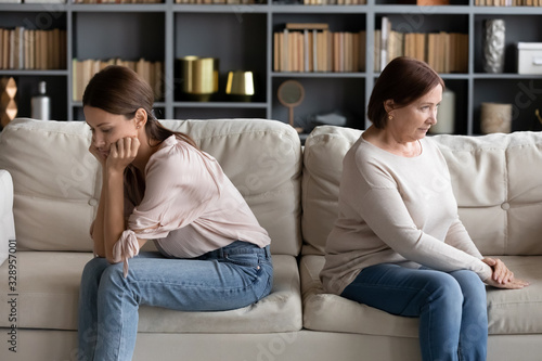 Foto Stressed young woman sitting separately with offended mature old mother in living room