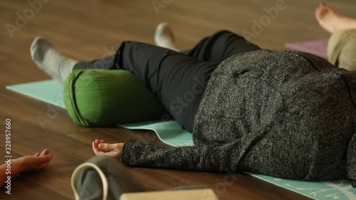 Selective focus of senior female in corpse pose with knees resting on bolster doing breathing exercise at yoga session to cure breast cancer photo