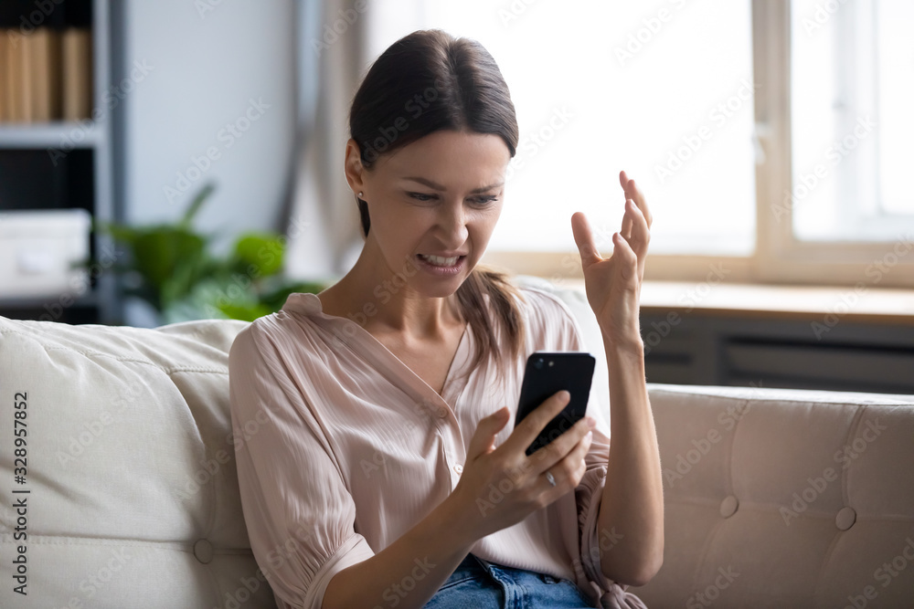 Annoyed young woman looking at mobile phone screen, feeling nervous. Angry lady irritated by bad device work, low wifi internet connection, scam spam message, forgot password or missed data. Annoyed young woman looking at mobile phone screen, feeling nervous. Angry lady irritated by bad device work, low wifi internet connection, scam spam message, forgot password or missed data.