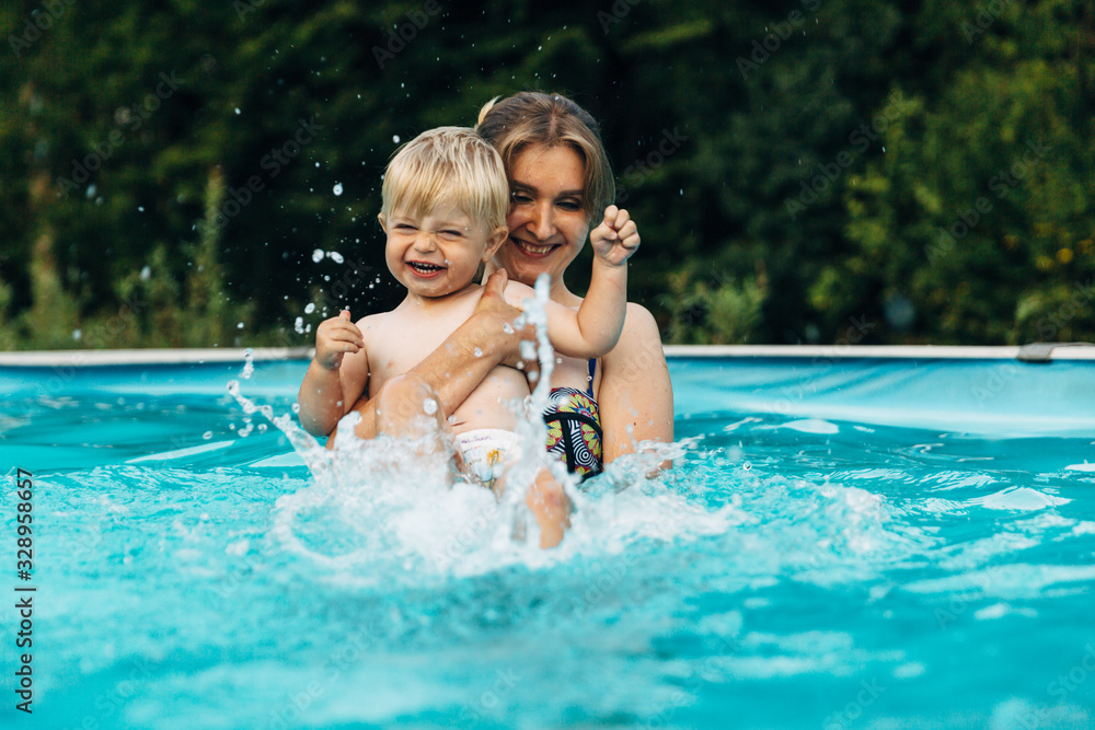 Mother and son having fun with splashes in outdoor swimming pool. Mother's Day.