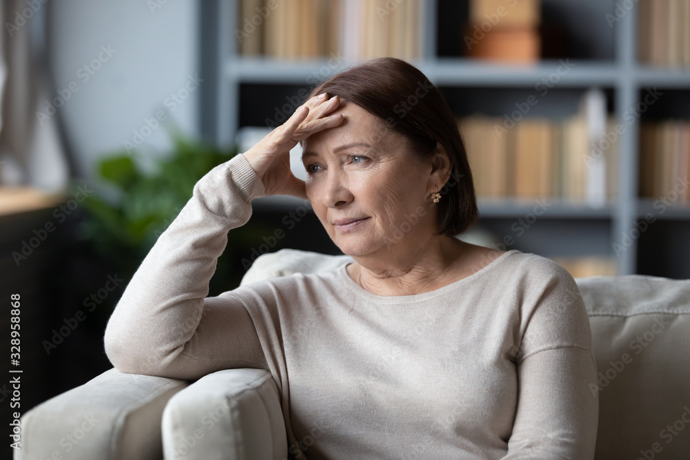 Stressed senior retired woman touching forehead, looking away, feeling doubtful about decision. Unhappy thoughtful middle aged lady sitting on couch, worrying about personal problems alone at home. Stressed senior retired woman touching forehead, looking away, feeling doubtful about decision. Unhappy thoughtful middle aged lady sitting on couch, worrying about personal problems alone at home.